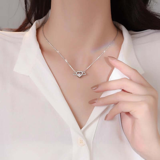 Woman wearing S925 sterling silver angel heart necklace with cross chain, featuring wing and heart design. Ethical, affordable jewelry.